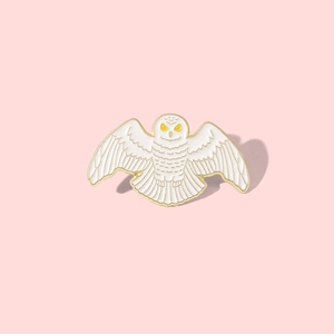 Exquisite owl enamel pin with gold detailing and wings spread on a pink background