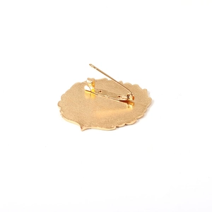 Golden metal crest brooch back view featuring a safety pin clasp and matte finish texture