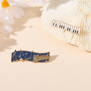 Detail of enamel music brooches featuring piano keys and a cat with golden notes