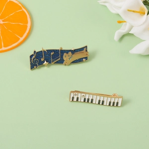Enamel pins featuring a starry sky music note cat and piano keys with golden paw prints
