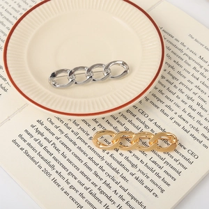 Minimalist gold and silver link chain brooches on a ceramic plate with vintage books