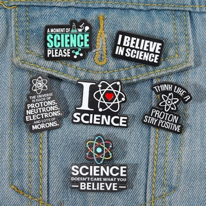 Close-up of six science enamel pins with atom designs on a blue denim jacket