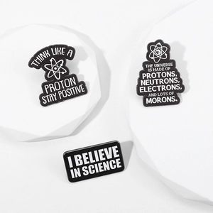 Close-up of three black and white science enamel pins on white geometric stone blocks