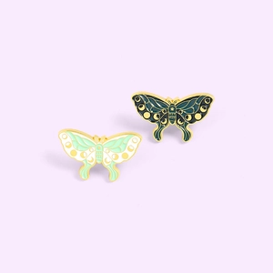 Cartoon enamel butterfly pins featuring moon phase designs on green and cream wings