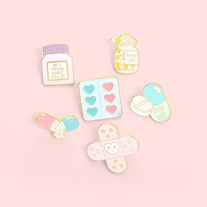Cartoon medical enamel pins set with happy pill and band-aid designs on pink backdrop