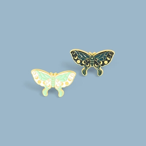 Detail of moth enamel pins featuring moon phases on mint and dark green wings
