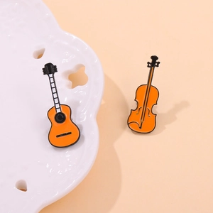Detailed macro shot of vibrant orange enamel guitar and violin brooches on ceramic