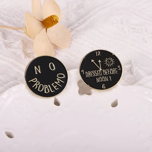Detail of two black enamel pins with funny slogans on white decorative ceramic tray