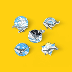 Set of five artistic whale enamel pins featuring ocean and galaxy designs on yellow background