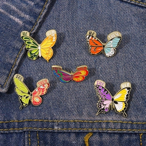 Détail de pin's papillons émaillés colorés avec pronoms sur du tissu denim bleu