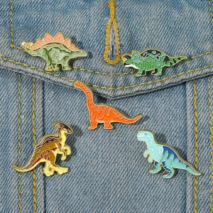 Lot de cinq épingles en émail dinosaures colorés sur tissu denim montrant divers types