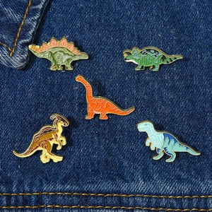 Détails de broches dinosaures colorées en émail fixées sur un tissu en jean bleu foncé
