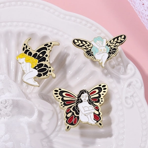 Close-up of three colorful butterfly girl enamel pins displayed on white ceramic plate