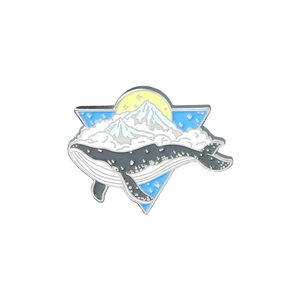 Artistic enamel whale badge with snowy mountains and crescent moon on white backdrop