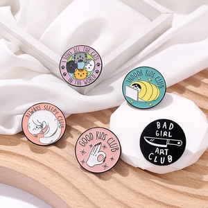 Five round cartoon cat club enamel pins with slogans on a wooden and fabric backdrop