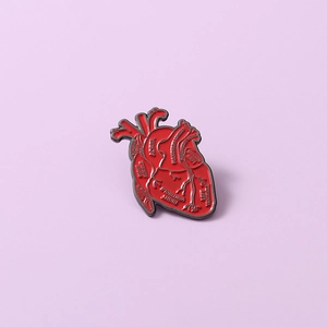 Macro detail of red anatomical heart enamel brooch with scientific aorta labels