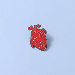 Macro shot of red anatomical heart enamel pin with detailed medical anatomy terminology