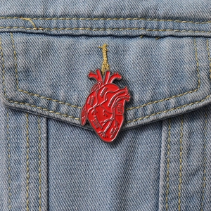 Detail of anatomical heart enamel pin with medical labels on a blue denim jacket pocket