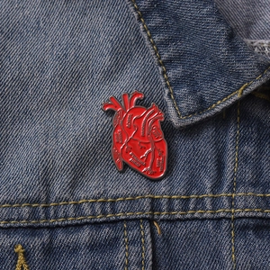 Anatomical red heart enamel pin with aorta and ventricle labels on blue denim fabric