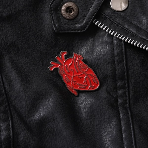 Macro detail of red anatomical heart enamel pin with white medical terminology labels