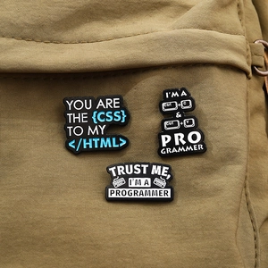 Three metal programmer pins with coding quotes pinned on a brown canvas backpack