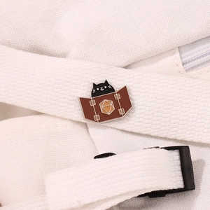 Cute black cat enamel pin with a d20 dice screen on a white fabric bag strap