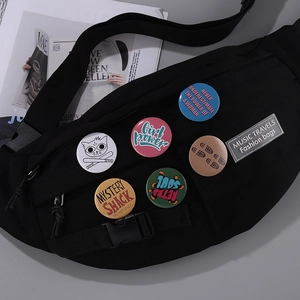 Detail of colorful tinplate badges on a black canvas crossbody bag with slogan pins