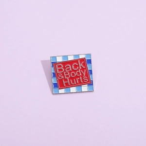 Macro shot of square enamel pin featuring Back and Body Hurts text with checkered border