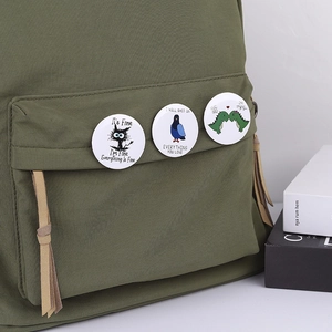 Tinplate cartoon cat and dinosaur badges pinned on a green canvas bag pocket