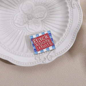 Square enamel brooch with Back & Body Hurts quote on red background and checkered border