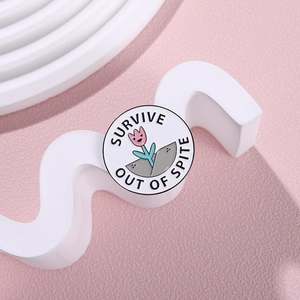 Round floral enamel pin with Survive Out Of Spite slogan on pink textured background