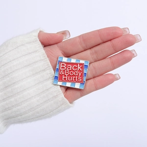 Funny enamel brooch pin with Back & Body Hurts text and blue plaid pattern on white sweater