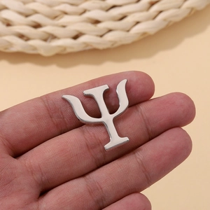 Macro view of a silver-toned metal Psi symbol pin held in hand to show scale and polish