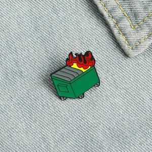Nahaufnahme einer grünen Mülltonnenbrand-Emaille-Anstecknadel auf blauem Denim-Hintergrund