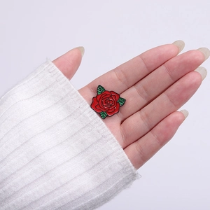 Spilla in smalto rosa rossa con foglie verdi sulla mano, regalo creativo per donna