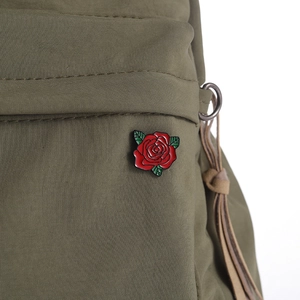 Dettaglio di spilla smaltata con rosa rossa su borsa in tessuto verde oliva con metallo