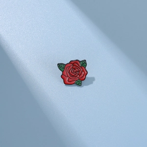 Dettaglio di una spilla in smalto a forma di rosa rossa con foglie verdi e contorni neri