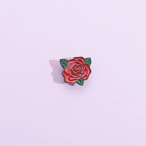 Dettaglio macro della spilla in smalto a forma di rosa con petali rossi e foglie