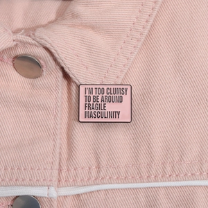 Pink enamel brooch with 'Fragile Masculinity' quote pinned on pink denim jacket