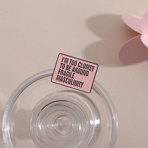 Macro detail of pink enamel pin with black slogan I'm too clumsy to be around fragile masculinity