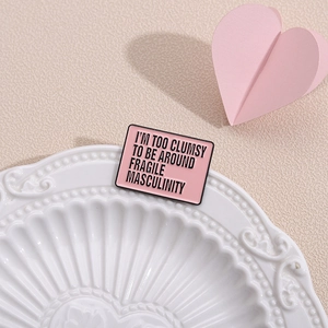 Pink enamel slogan brooch on a ceramic plate featuring fragile masculinity quote