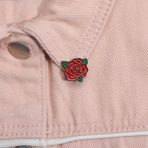 Dettaglio di una spilla smaltata a forma di rosa rossa sul colletto di una giacca rosa