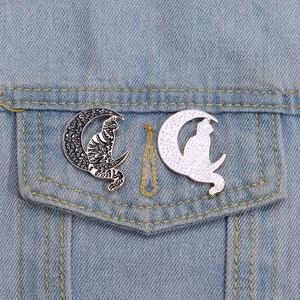 Black and white cat sitting on crescent moon enamel pins on blue denim jacket pocket