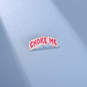 Macro detail of Choke Me enamel pin with pink dripping liquid font and silver base