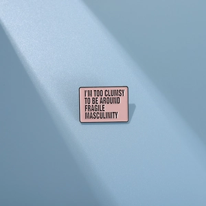 Rectangular pink enamel pin with black metal edges featuring minimalist English text design