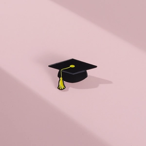 Minimalist black enamel graduation cap pin with yellow tassel on a pink background