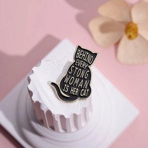 Creative black cat enamel brooch with golden lettering on a marble display stand