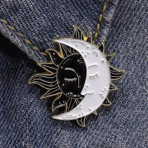 Detail of sun and moon enamel pin with gold edging on blue denim fabric texture