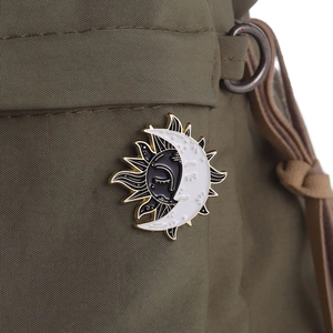 Enamel brooch with sun and moon design pinned on a green canvas bag strap