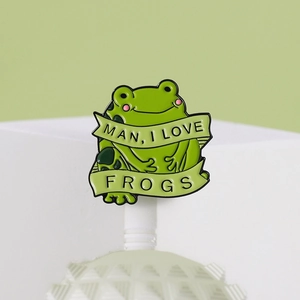 Cute green enamel frog pin with Man I Love Frogs banner on a clean white display stand